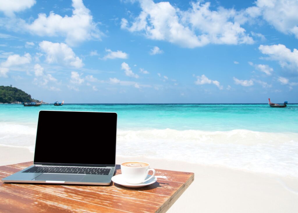 mesa com notebook e xícara em praia com mar e céu azul no fundo