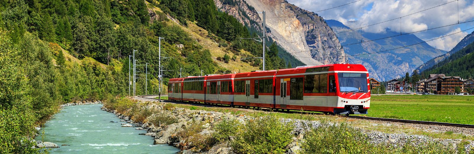 trem com montanha ao fundo e rio ao lado